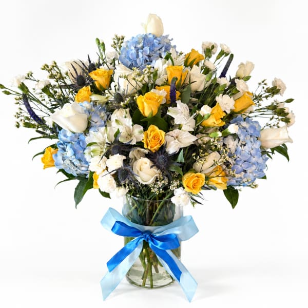 Bouquet of yellow and white roses with blue hydrangeas in a glass vase