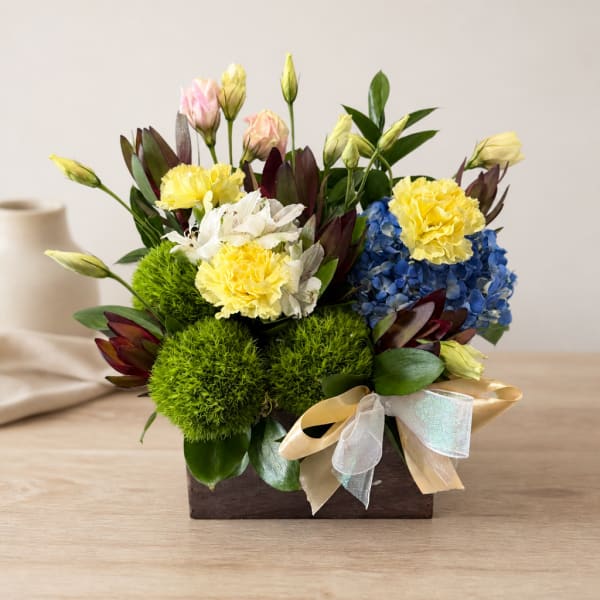 Mixed bouquet in a wooden box with yellow, blue, pink, and white blooms