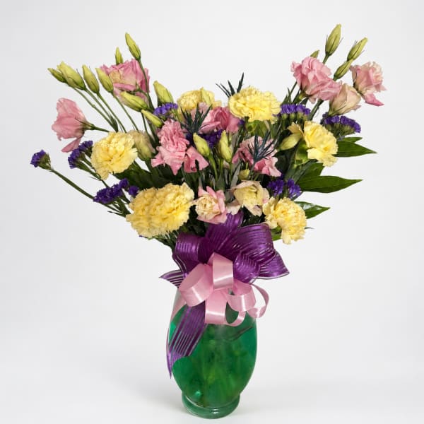 Pink and yellow mixed bouquet in a green glass vase with purple ribbon