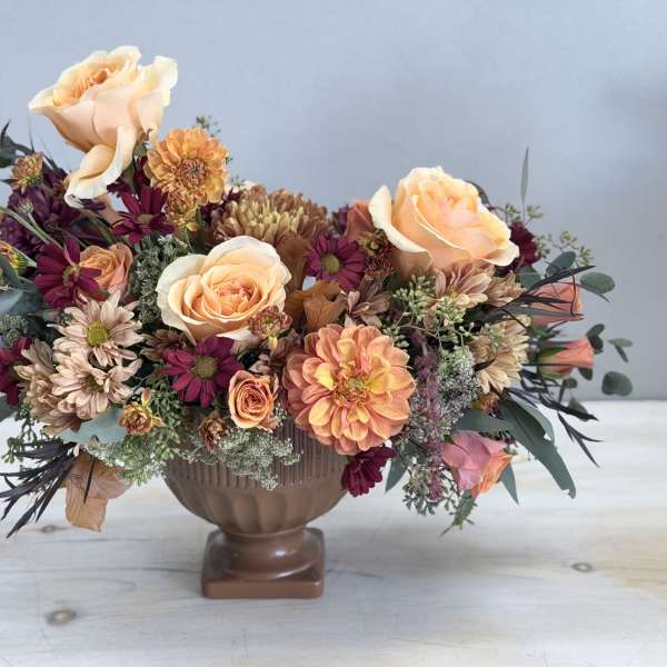 Low centerpiece of peach roses and mixed autumn flowers in a brown pedestal bowl