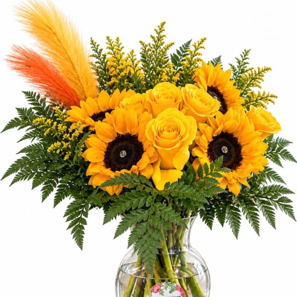 Yellow roses and sunflowers in a clear glass vase with orange and yellow feathers