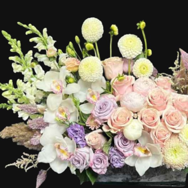 Pastel floral arrangement with roses, orchids, and round white blooms in a low container