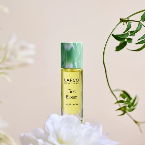 A perfume bottle labeled LAFCO New York First Bloom with white flowers around it.