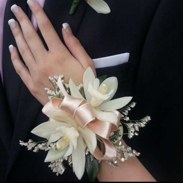 White floral corsage and boutonniere on a black suit with pink ribbon