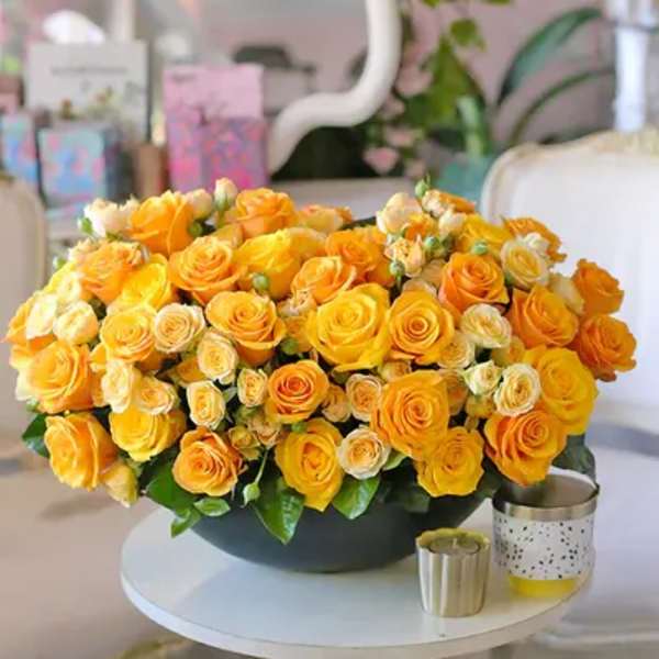 Large bouquet of yellow and orange roses in a dark bowl on a white table