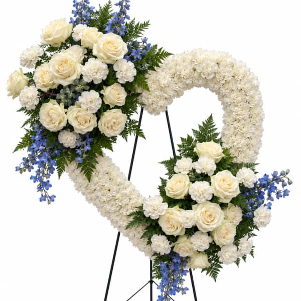 Heart-shaped floral wreath with white roses and blue flowers on a stand
