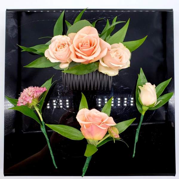 Peach rose boutonniere set with green leaves on a black tray