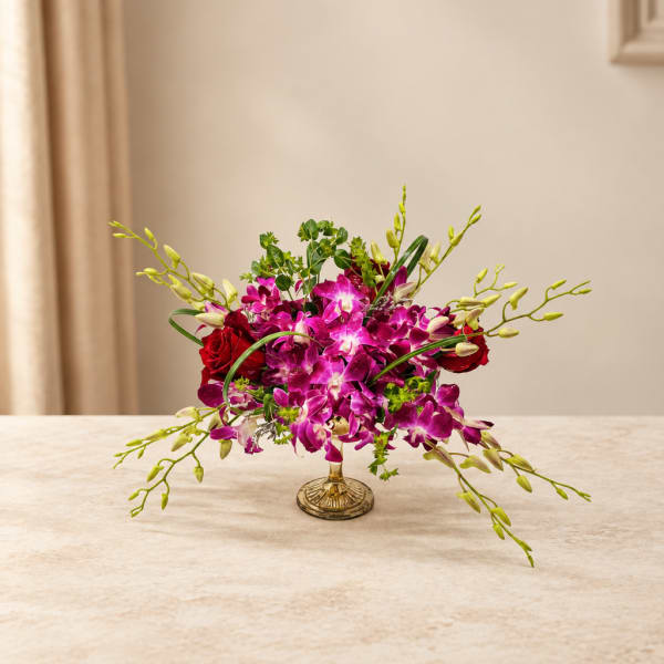 Purple orchids and red roses arranged in a gold pedestal vase