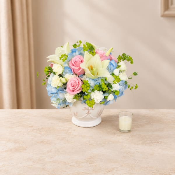 Bouquet of pink roses, white lilies, and blue hydrangeas in a white vase