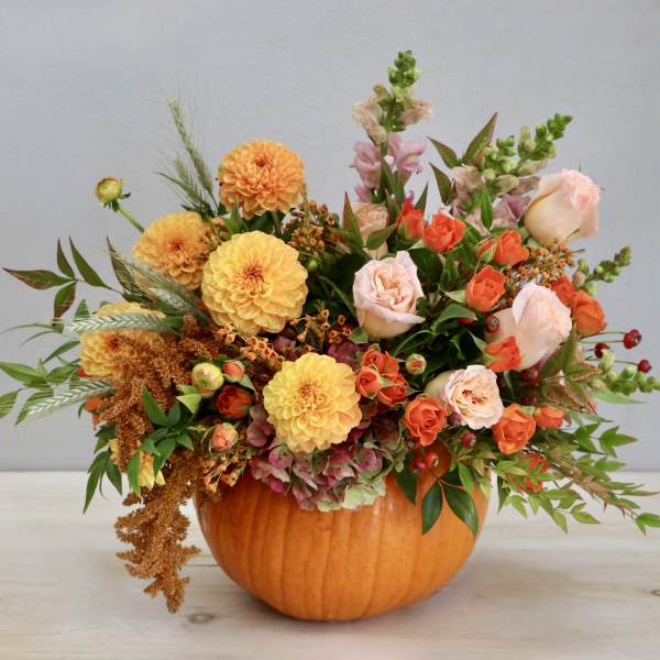 Autumn arrangement of orange and peach flowers in a hollow pumpkin container