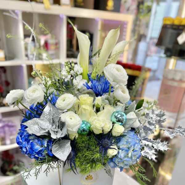 Box arrangement of white calla lilies, roses, and blue hydrangeas with silver accents in a white square container