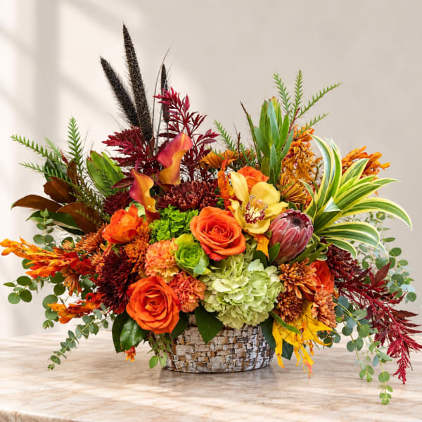 Autumn floral arrangement in a woven basket with orange and red blooms