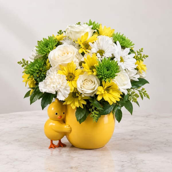 Yellow and white flower arrangement in a yellow vase with a chick figurine