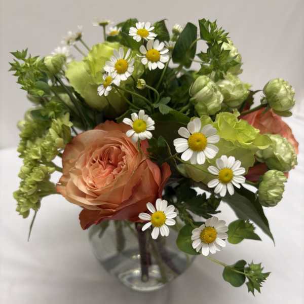 Small peach rose and white daisy arrangement with green accents in a round clear glass vase.