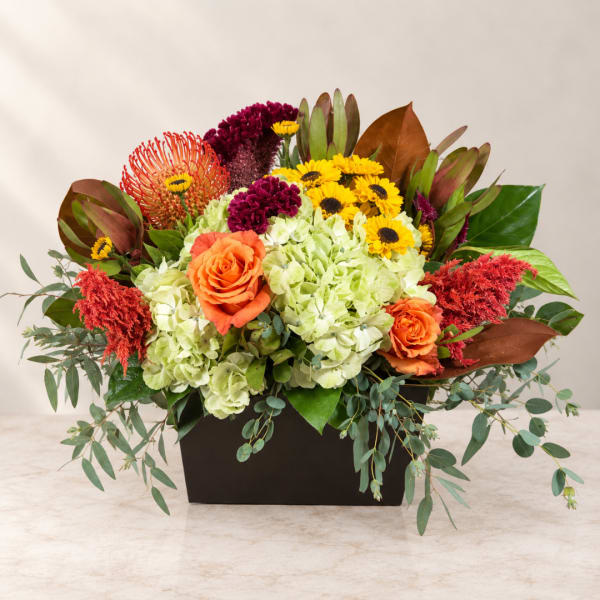 Mixed floral arrangement in a black rectangular container with orange roses and yellow blooms