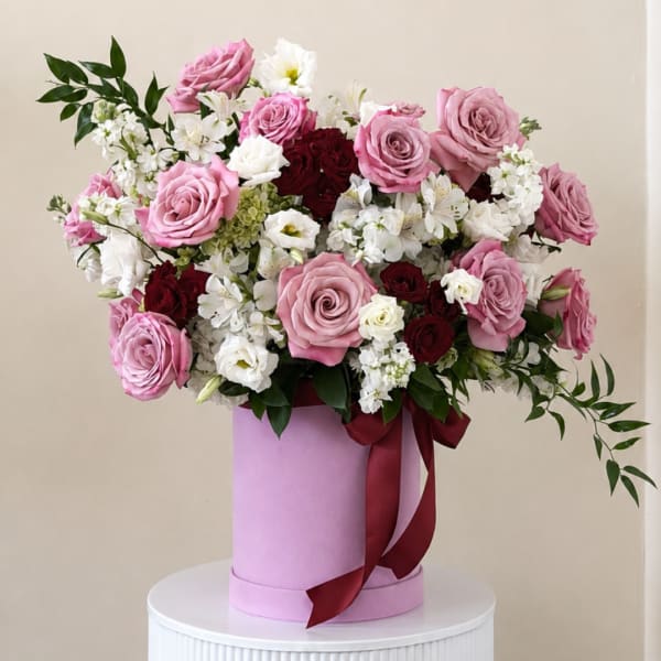 Pink and white rose arrangement in a lavender hat box with a burgundy ribbon
