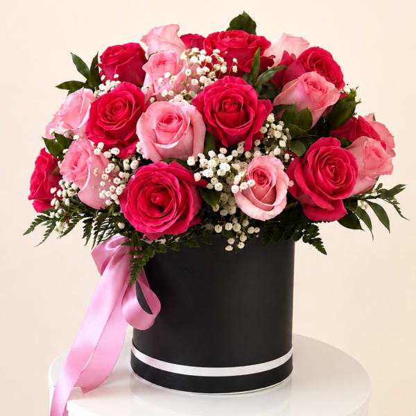 Pink and red roses arranged in a black hatbox with a pink ribbon