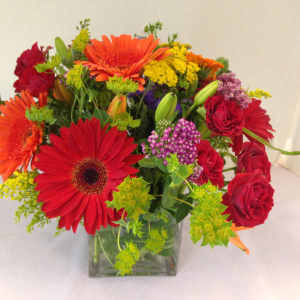 Mixed bouquet of red and orange flowers in a clear square vase
