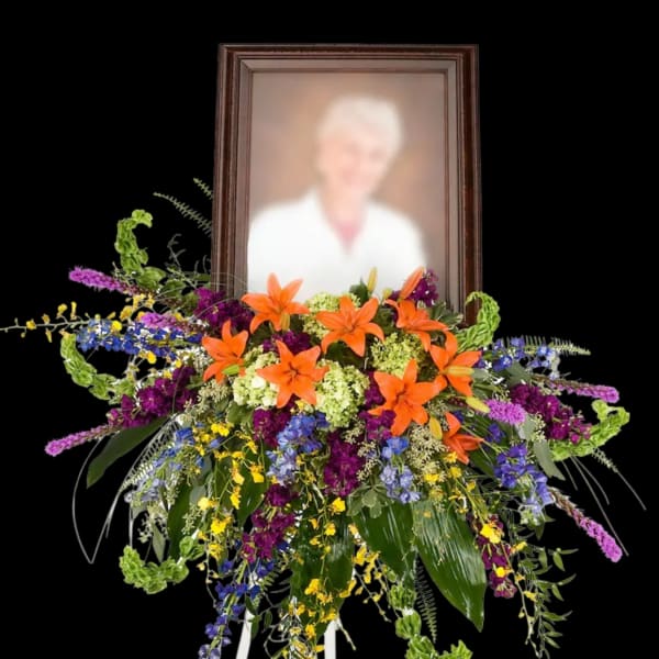 Standing floral spray with orange lilies and a framed portrait