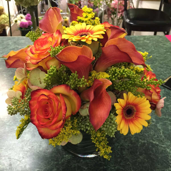 Orange roses, calla lilies, and yellow gerbera daisies in a glass vase