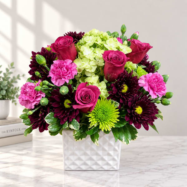 Pink roses, carnations, and dark mums in a white square vase