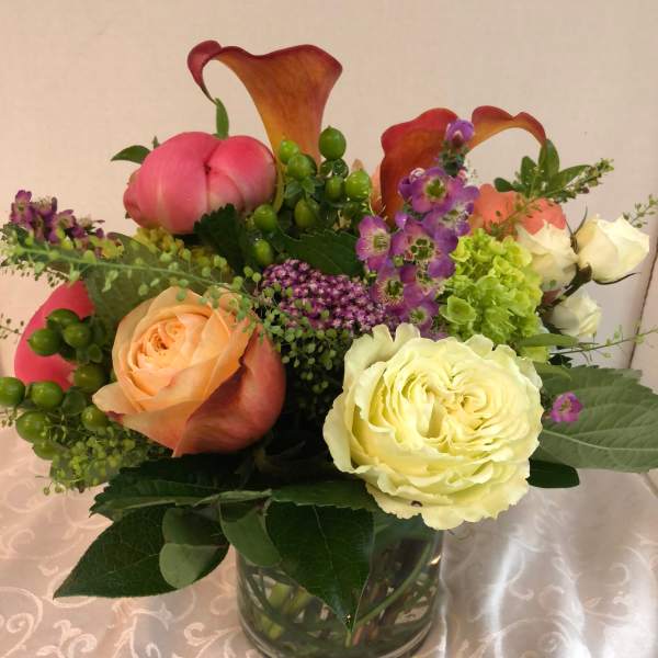 Mixed bouquet in a glass vase with roses, calla lilies, and purple accent flowers