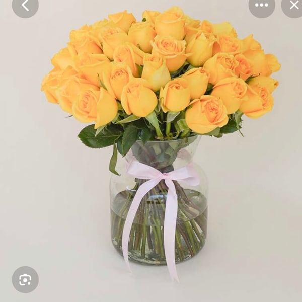 Yellow roses in a clear glass vase with a pink ribbon