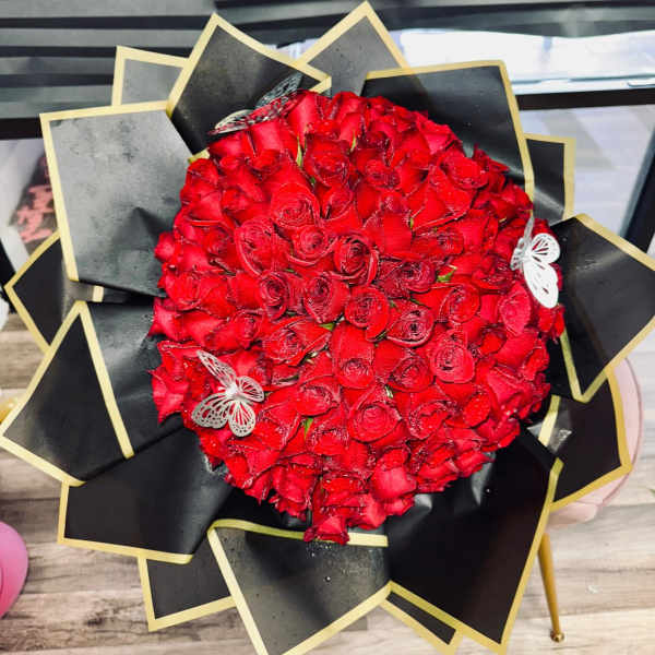 Round bouquet of red roses wrapped in black paper with gold trim