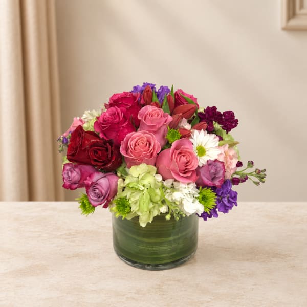 Mixed bouquet of pink, red, white, and purple flowers in a green glass vase