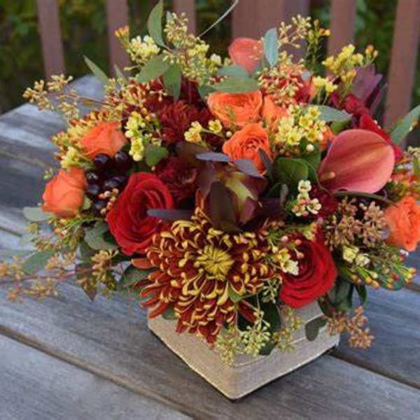 Mixed bouquet of red, orange, and pink flowers in a square vase