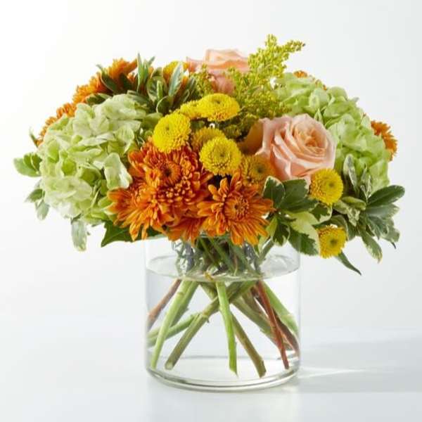 Orange and yellow flowers in a clear glass vase with pale pink roses