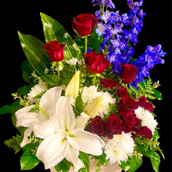 Bouquet of red roses, white lilies, and blue flowers in a low container