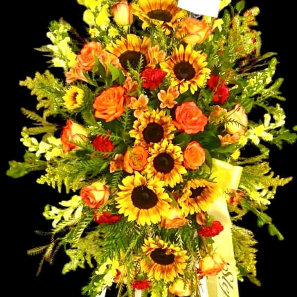 Tall floral standing spray with sunflowers and orange roses on a black background