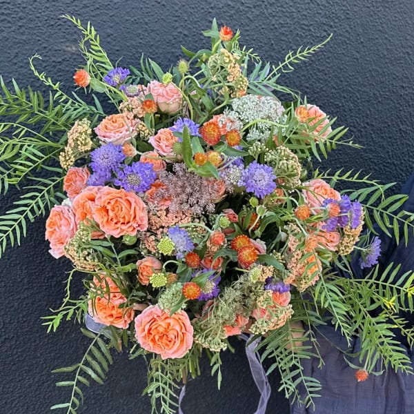Round bouquet of peach roses and purple flowers with airy greenery.
