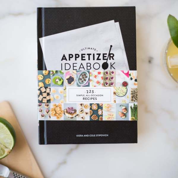 A cookbook on a marble surface with glasses of drink around it