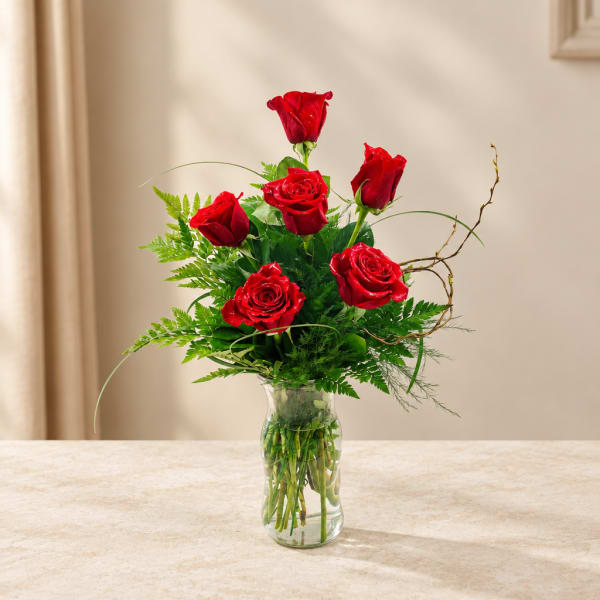 Red roses arranged in a clear glass vase with greenery