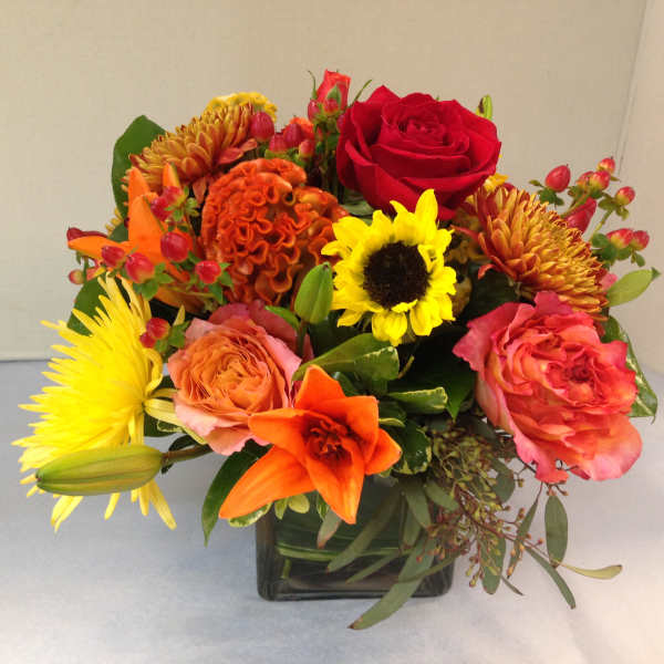 Mixed bouquet in a square glass vase with roses, lilies, and sunflowers