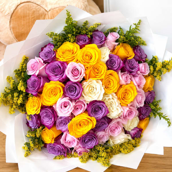 Bouquet of yellow, purple, pink, and white roses wrapped in white paper