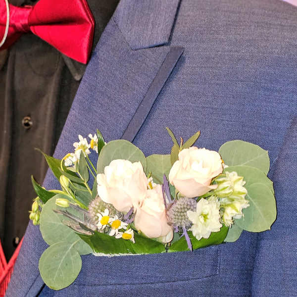 Boutonniere with pale roses and small white flowers on a blue suit jacket