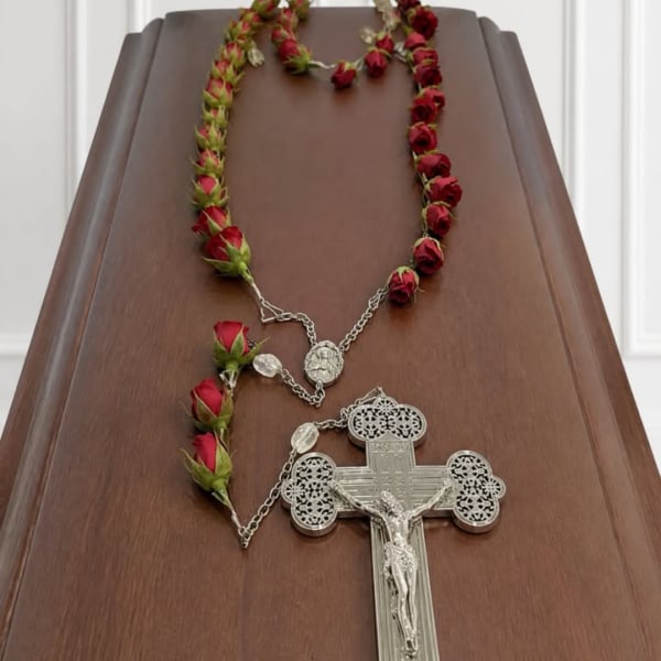Red rose rosary laid on a wooden surface with a silver crucifix