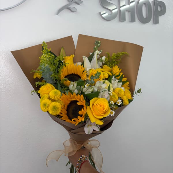 Yellow bouquet with sunflowers, roses, and white lilies wrapped in brown paper