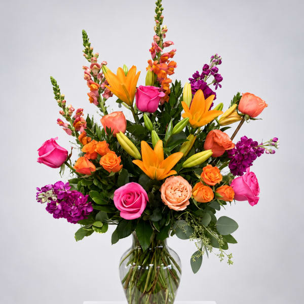 Bright mixed bouquet with roses, lilies, and purple blooms in a glass vase