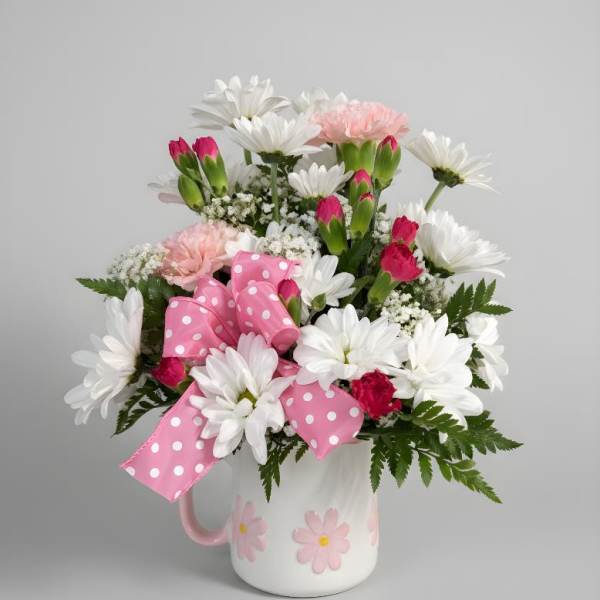 Pink and white flower arrangement in a white mug with a polka-dot bow