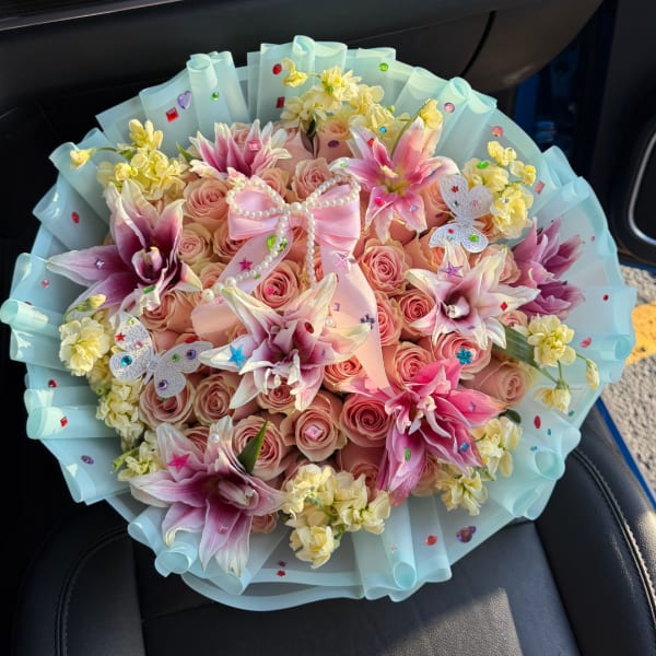 Pink rose bouquet with lilies, yellow filler flowers, and a ribbon bow