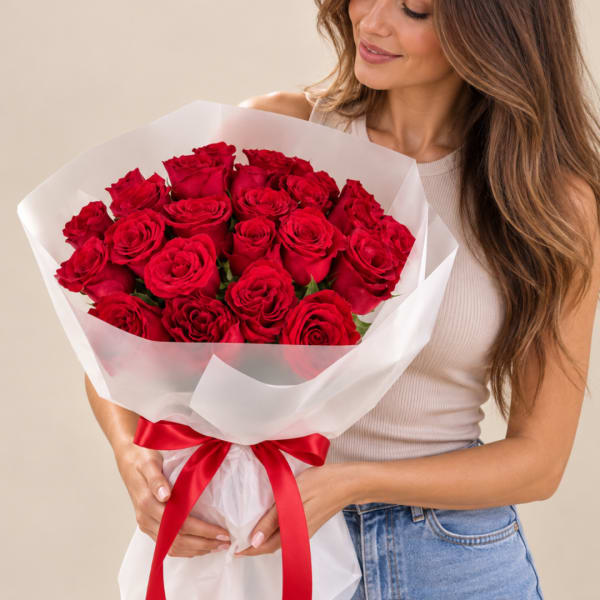 Woman holding a bouquet of red roses wrapped in white paper with a red ribbon.