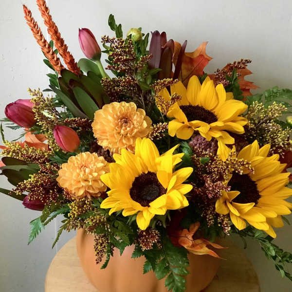 Autumn bouquet with sunflowers, tulips, and orange blooms in a pumpkin-colored vase.