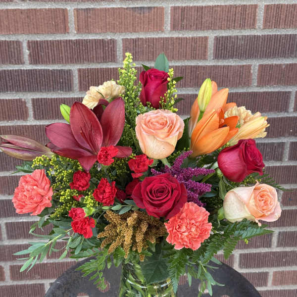 Mixed bouquet of roses, lilies, and carnations in a glass vase