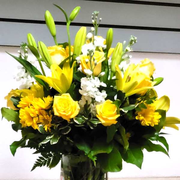 Yellow roses and lilies arranged in a clear glass vase