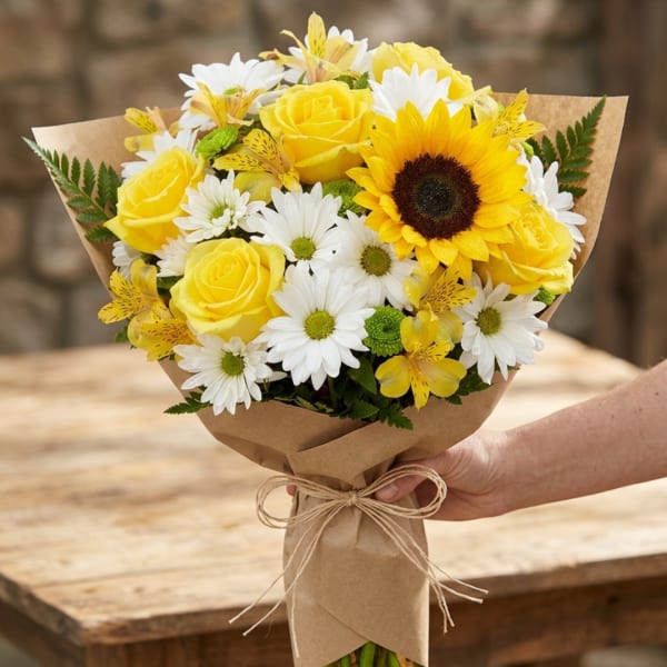 Bouquet of yellow roses, white daisies, and a sunflower wrapped in kraft paper