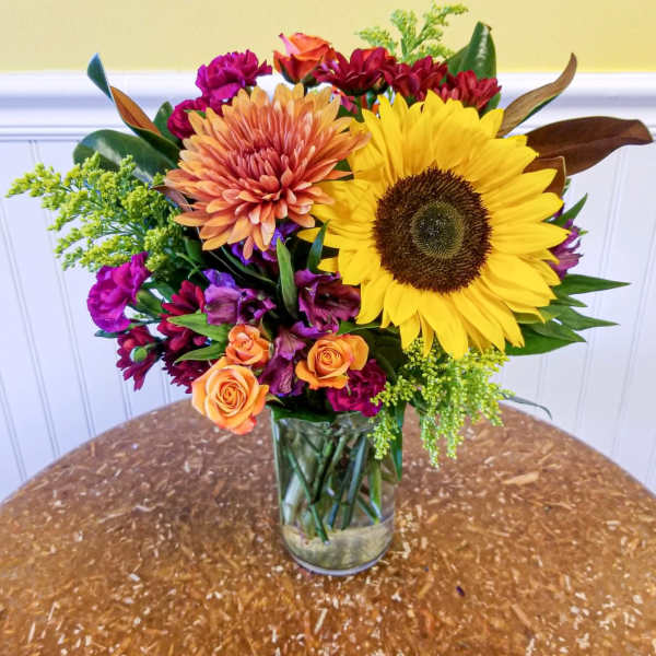 Mixed bouquet in a clear glass vase with a large sunflower and orange blooms